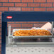A person in gloves putting french fries on a tray in a Hatco countertop hot food display warmer.