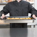 A chef holding a Vollrath stainless steel steam table pan full of food.
