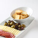 A Tuxton bright white slanted china bowl on a table with a plate of olives, cheese, and crackers.