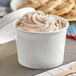 A white Choice paper food cup filled with ice cream and cookies with a vented lid on a counter.