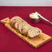 An American Metalcraft olive wood serving board with sliced bread and butter next to it.