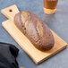 An American Metalcraft olive wood serving board with a loaf of bread and a glass of wine.