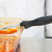 A chef uses a knife to cut food in a glass container with a Vollrath black spoodle handle.