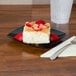 A piece of cake on a Fineline black plastic dessert plate with strawberries on top.