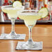Two Acopa margarita glasses filled with yellow liquid and garnished with lime slices.