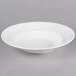 A Tuxton San Marino AlumaTux Pearl White china bowl with a curved edge on a gray surface.