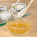A Libbey Winchester glass ramekin filled with dipping sauce with chopsticks holding a sushi roll.