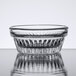 A clear Libbey Winchester glass ramekin with a patterned rim on a reflective surface.