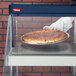 A hand in a glove placing a pizza in a Hatco Glo-Ray countertop warmer.