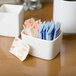 A white Tuxton china sugar packet holder on a white surface filled with sugar packets.