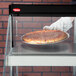 A hand in a glove using a Hatco countertop glass oven to hold a pizza.
