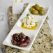 A rectangular white china plate with 3 compartments holding olives, feta cheese, and wine.