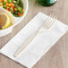 A Visions beige heavy weight plastic fork on a white napkin next to a bowl of vegetables.