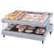 A Hatco white heated glass merchandising warmer with food trays on a slanted shelf.