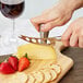 A person using a Franmara stainless steel cheese knife to cut cheese on a cutting board.