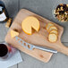 A Franmara stainless steel cheese knife on a cutting board with cheese, crackers, and a wine glass.