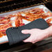 A person using a black San Jamar Ultigrips hot pad to hold a bacon pan.