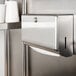 A Bobrick stainless steel surface-mounted paper towel dispenser on a wall.