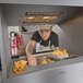 A man in a white apron and cap using a Hatco fry holding station to put french fries in a container.