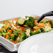 A black Cambro perforated salad bar spoon in a tray of broccoli and carrots.