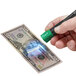 A hand uses a Dri Mark Dual Test UV Detector Pen on a dollar bill on a counter.