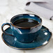 A blue Tuxton china cup on a saucer with a napkin.