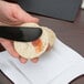 A person's hand holding a black Fineline plastic sandwich spreader and spreading jam on a piece of bread.