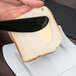 A person using a Fineline black plastic sandwich spreader to spread butter on a piece of bread.