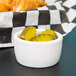 A white Tuxton porcelain ramekin filled with pickles on a counter.