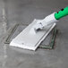A person using a Unger white scrub pad with a green handle to clean a floor.