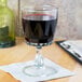 An Arcoroc wine glass filled with red wine on a napkin next to a bottle of wine.