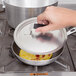 A hand using a Vollrath domed aluminum pot/pan cover over a pan of food.