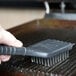 A person cleaning a metal surface on a Waring panini grill with a brush.