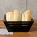 A black square tapered birch bread basket on a table with loaves of bread.