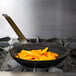 A Vollrath French style carbon steel fry pan with food in it on a stove.