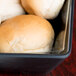 A black American Metalcraft bowl with white basket liners holding rolls of bread on a hotel buffet counter.