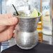A person holding an American Metalcraft stainless steel Moroccan tumbler with a drink and lime wedge in it.
