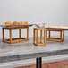 An American Metalcraft bamboo riser set with wooden trays of pastries on a table.