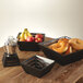 An American Metalcraft black square bread basket on a table with other black bread baskets and fruit.