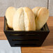 An American Metalcraft square birch bread basket on a table with loaves of bread.