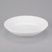 An Arcoroc white coupe bowl on a gray surface.