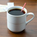 An Arcoroc stackable coffee mug filled with coffee and a red straw on a counter.