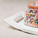 A jar of colorful sprinkles on a white rectangular porcelain platter with handles.
