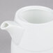 A close-up of a white Arcoroc teapot with a lid.