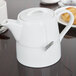 An Arcoroc white teapot with a cover on a table.