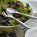 A bowl of salad with a Visions silver plastic serving fork and spoon.