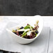 A white porcelain cradle bowl filled with salad topped with blueberries and grapes.