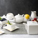 A 10 Strawberry Street white porcelain teapot on a table set with white dishes and fruit.