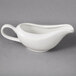A white gravy boat with a white spoon on a gray surface.