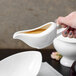A person using a 10 Strawberry Street white porcelain gravy boat to pour brown sauce into a white bowl.